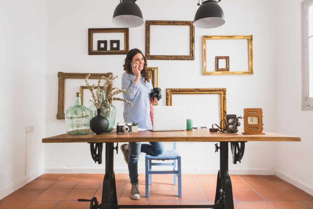 woman talking on the phone and holding a camera near the table, golden frames on the wall behind