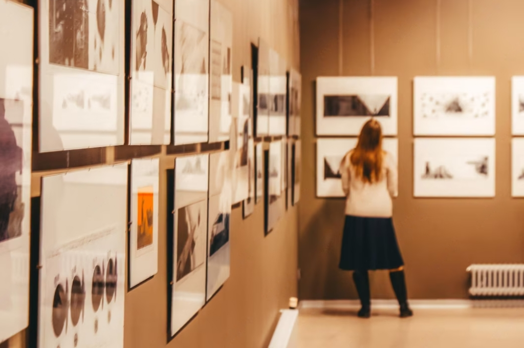 woman in black skirt and white sweater standing in the gallery with pictures on the wall