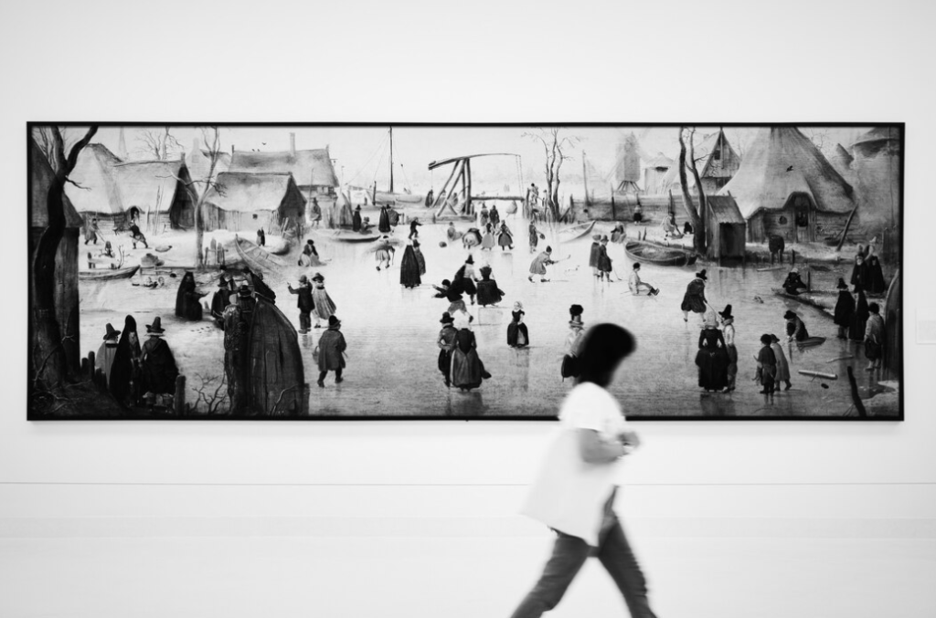 a silhouette of a blurred woman which passes by the black-and-white picture on the wall